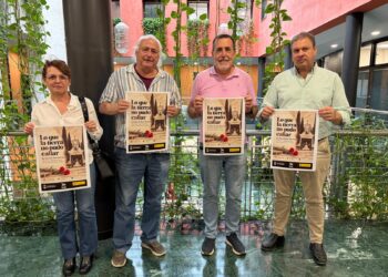 Cartel de la exposición sobre la memoria histórica en Dos Hermanas, con una fotografía del cementerio de San Pedro y claveles rojos.